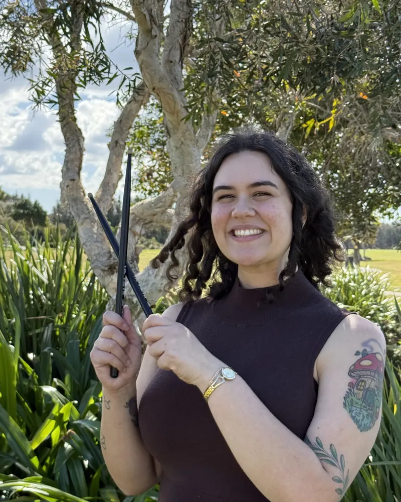 Steph smiling and holding a pair of drumsticks