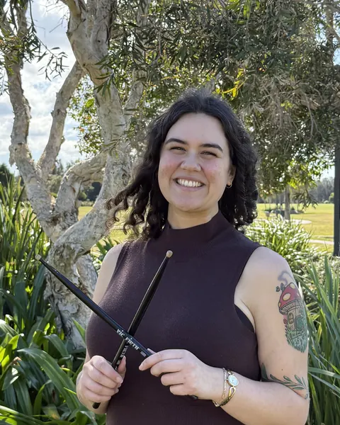 Steph smiling and holding drumsticks